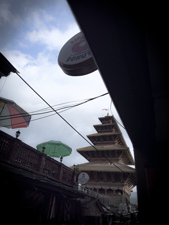 A tiered pagoda seen past a shopfront awning and umbrellas