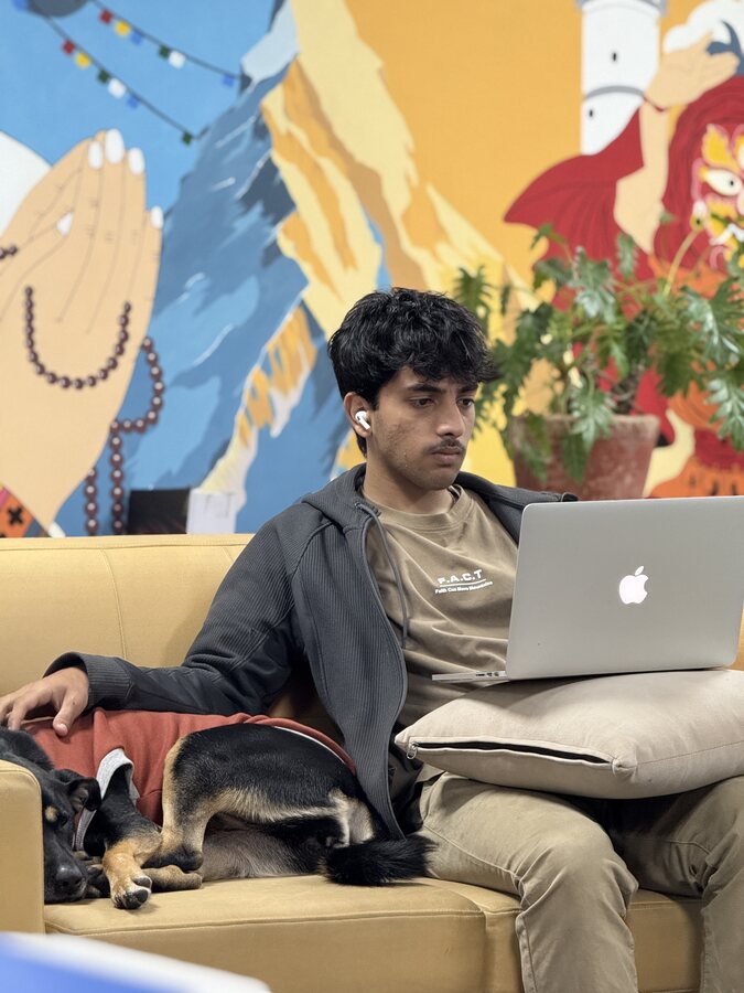 Aarohan on a couch with a laptop and a sleeping dog