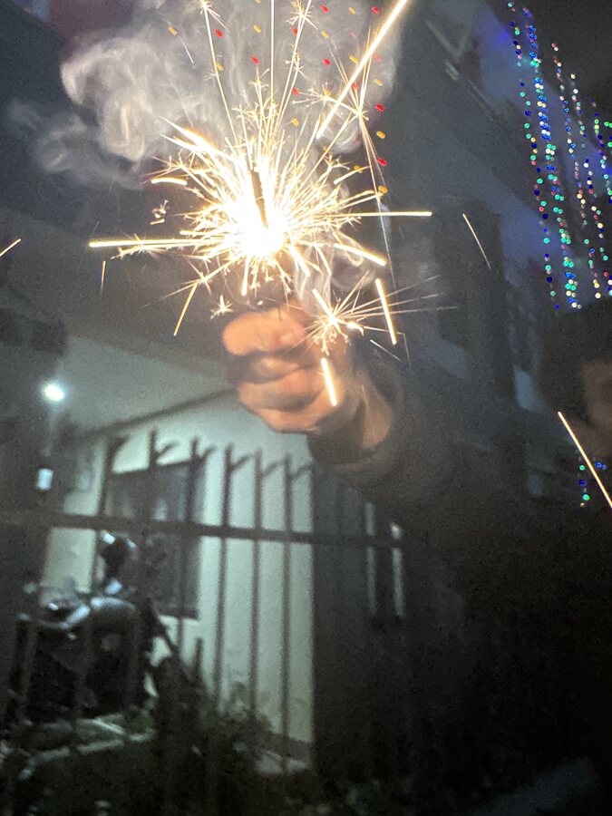 Holding a lit sparkler against a string of festival lights
