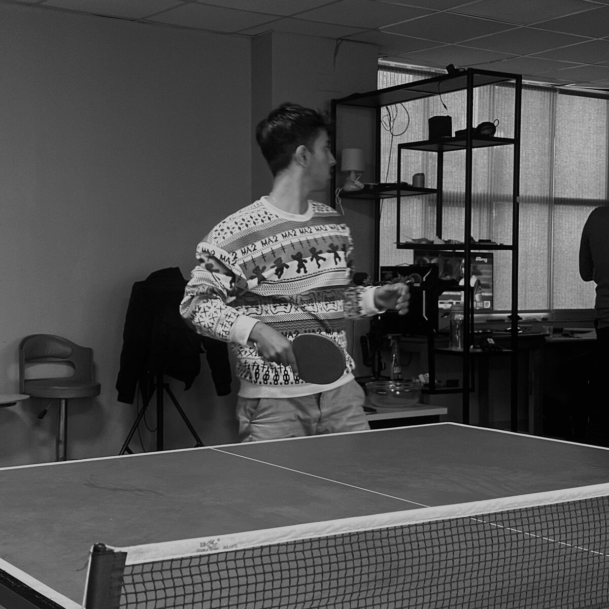 Mid-serve at a ping pong table, black and white