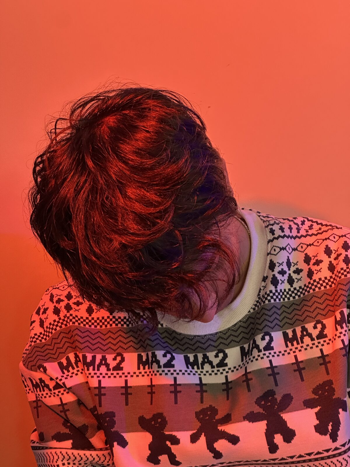Head bowed against a red wall, patterned sweater