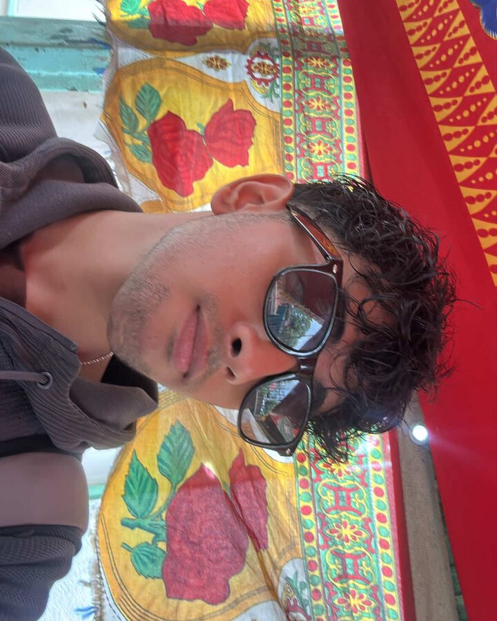 Lying sideways in sunglasses against embroidered Nepali cloth