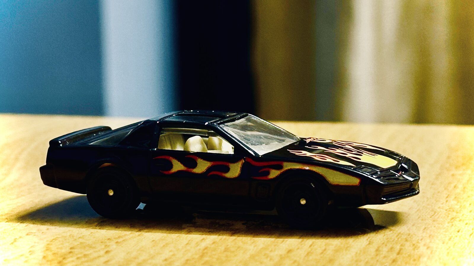 A die-cast car with flame decals, shallow focus on a wooden desk